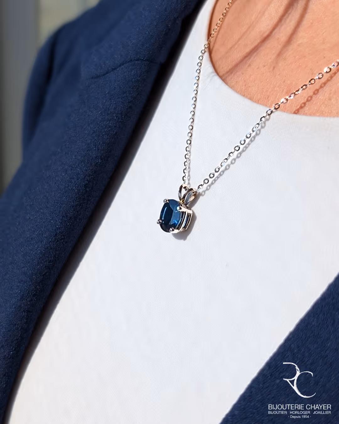 Collier en argent avec pendentif en pierre bleue porté sur un chemisier blanc et une veste bleue.