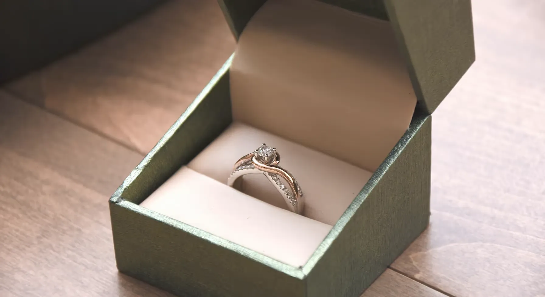 Bague en or avec diamant solitaire et petites pierres sur le côté dans une boîte à bijoux verte ouverte.