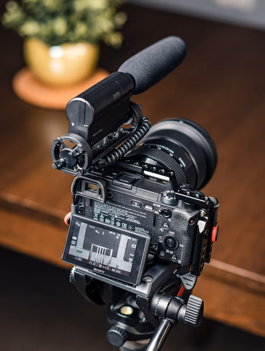 Caméra Sony avec microphone monté et écran LCD affichant les paramètres d'enregistrement, posée sur un trépied en bois.