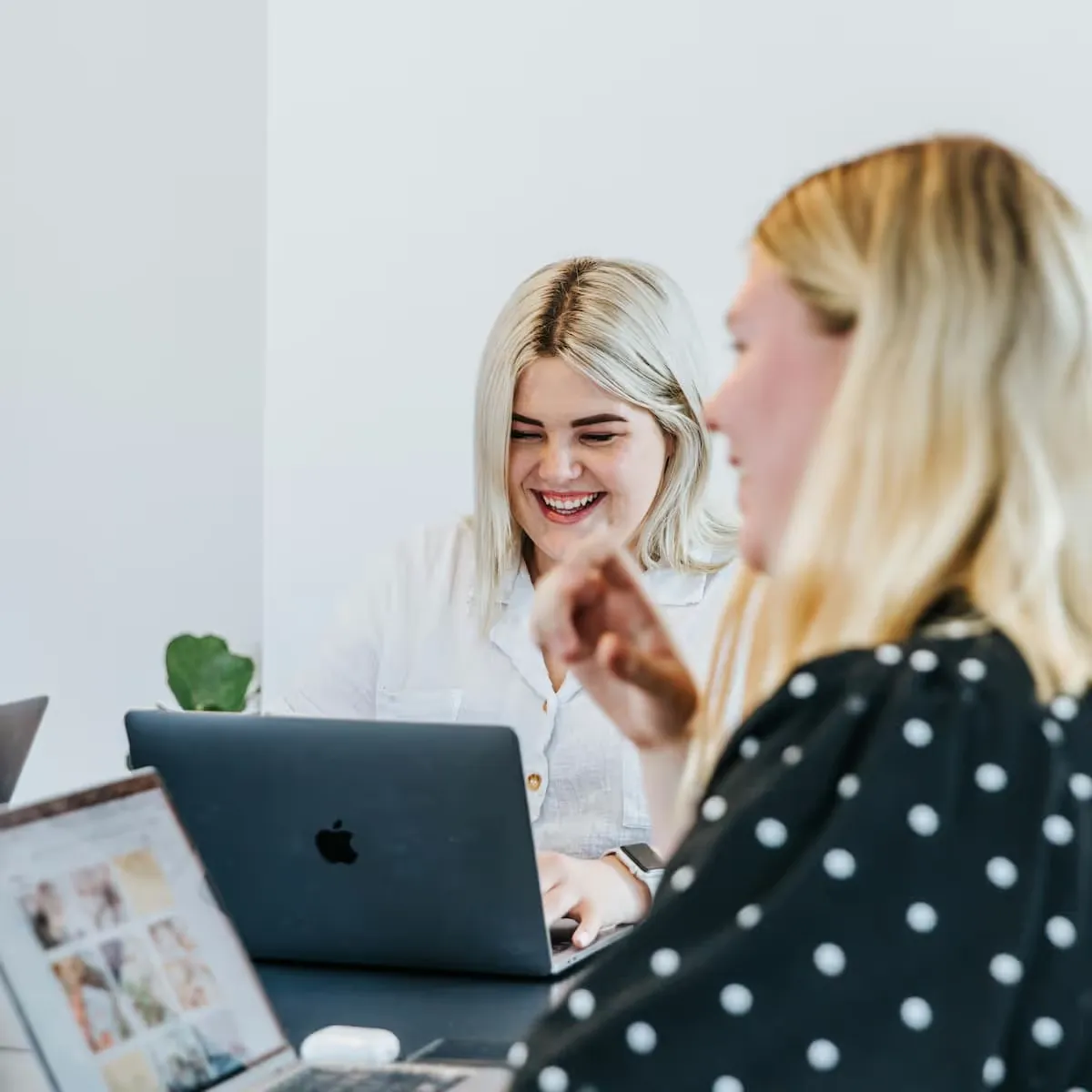 Deux femmes souriantes travaillant sur des ordinateurs portables dans un environnement lumineux.