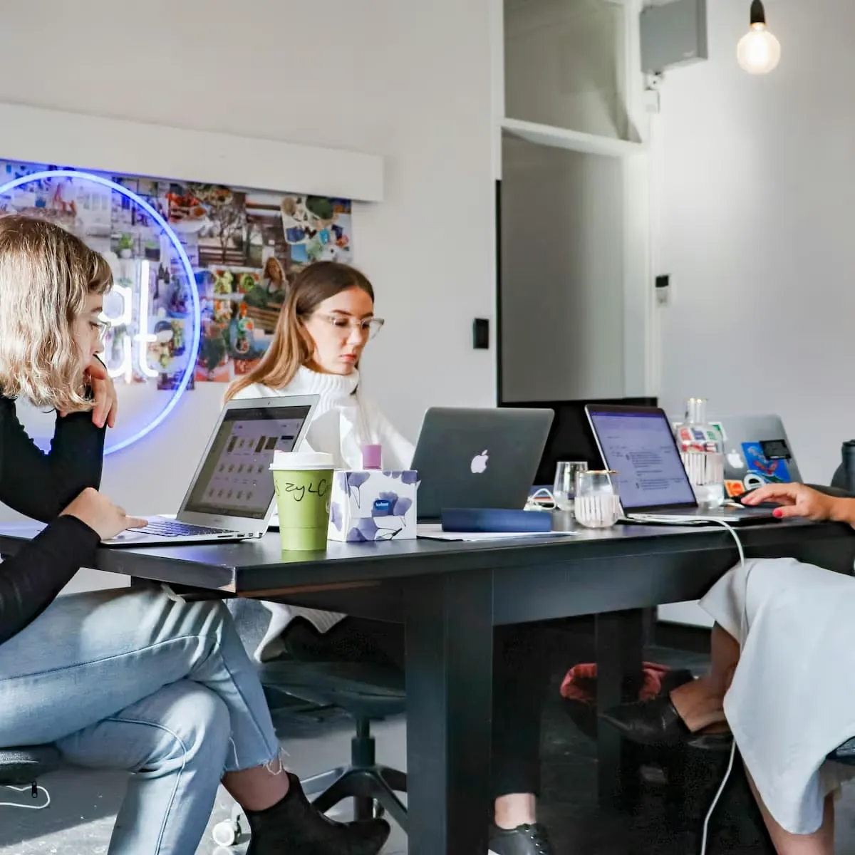 Trois personnes assises autour d'une table de travail avec des ordinateurs portables, dans un bureau moderne lumineux.