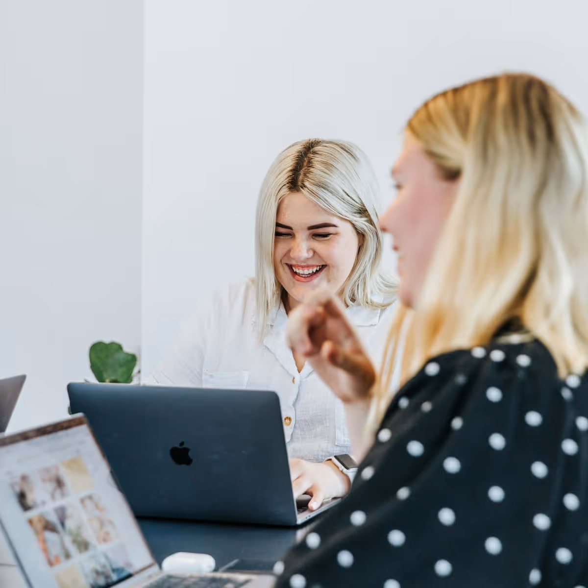 Deux femmes souriantes travaillant sur des ordinateurs portables dans un environnement lumineux.